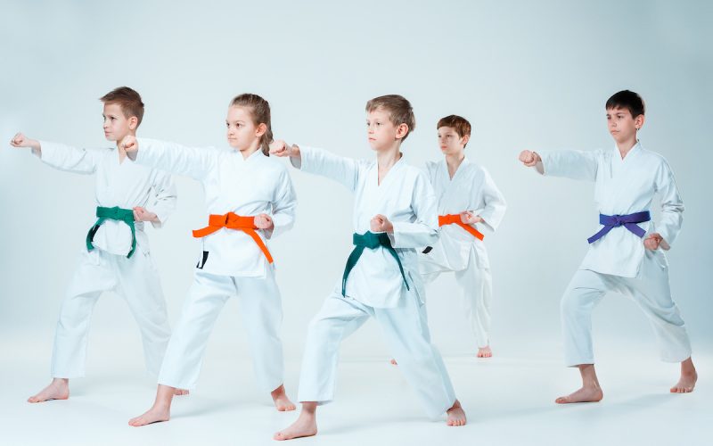 The teen boys and girl fighting at Aikido training in martial arts school. Healthy lifestyle and sports concept. Teenagers in white kimono on white background. Children with concentrated faces